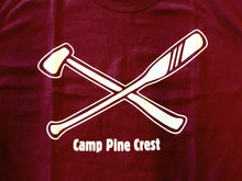 Maroon Adventure Leadership 2014 graphic close up. The image is a white screen print on maroon fabric featuring a graphic of an axe and paddle crossed in the shape of an X over the words Camp Pine Crest.